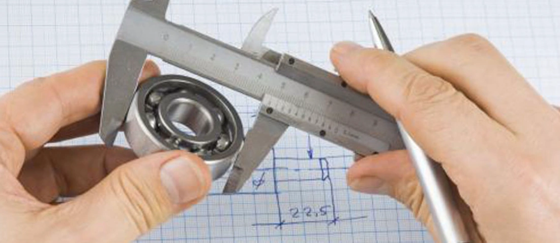 An image showing the measurement of dimensions of a bearing using a calliper as measurements are noted down on paper 