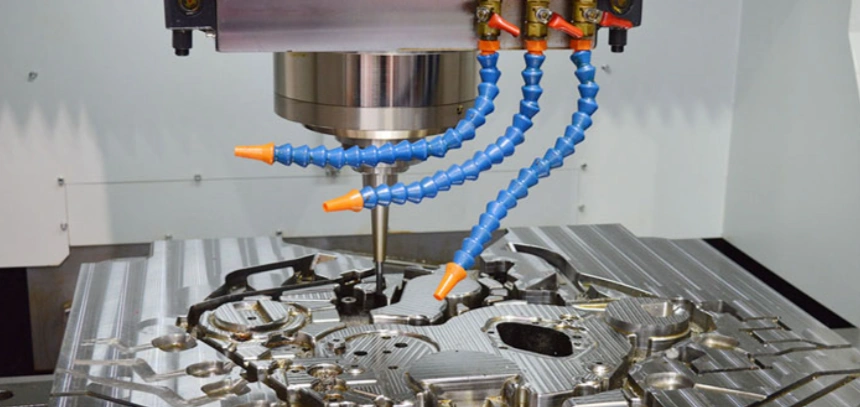 A close-up image of a 3-axis CNC machine creating curved cuts and holes on a metal block with three coolant nozzles  