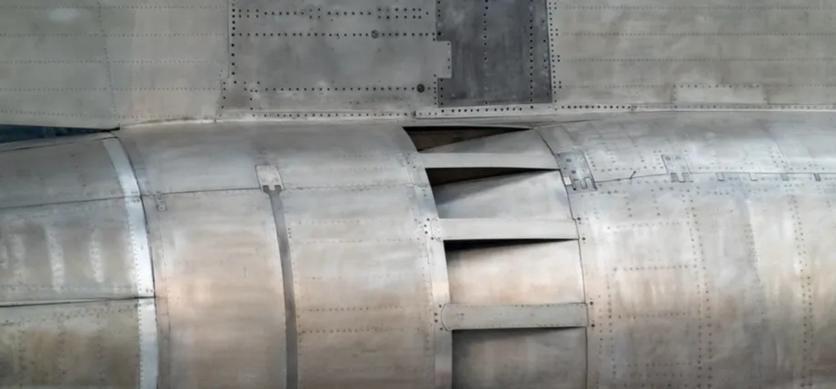 A detailed view of a large, curved aluminum structure featuring numerous rivets and metal panels typical of aerospace manufacturing