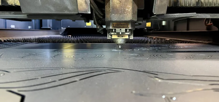 Fiber laser head actively cutting intricate patterns and text into a stainless steel sheet during precision sheet metal fabrication.