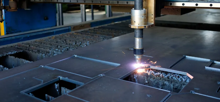 Plasma cutting torch emitting bright arc and sparks while precisely cutting rectangular openings in a thick steel plate during sheet metal fabrication.