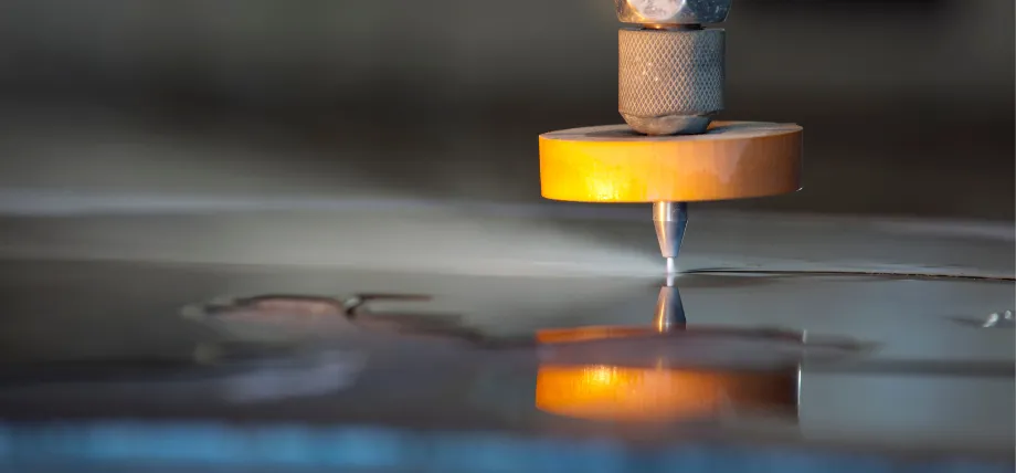 Waterjet cutting nozzle emitting a high-pressure abrasive water stream to precisely cut polished sheet metal during sheet metal fabrication.
