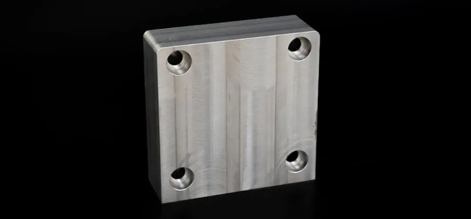 precisely machined rectangular aluminum block with a brushed finish, featuring four countersunk mounting holes at the corners