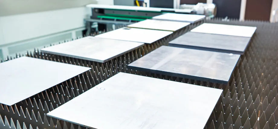 Several flat metal sheets arranged on a spiked support bed of a laser cutting machine.