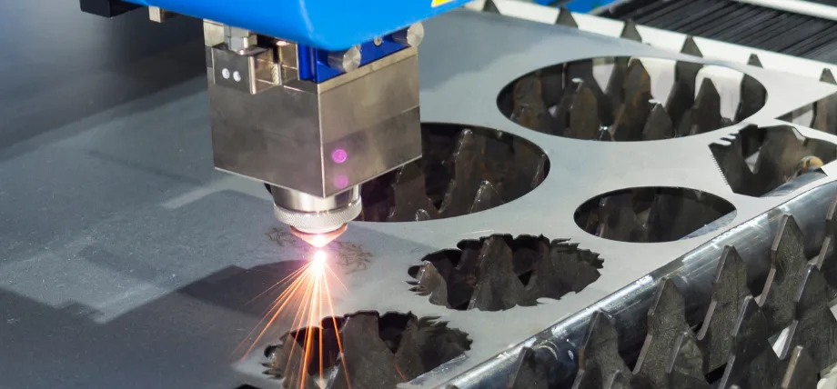 Laser head cutting detailed circular and irregular patterns into a metal sheet, producing bright sparks.