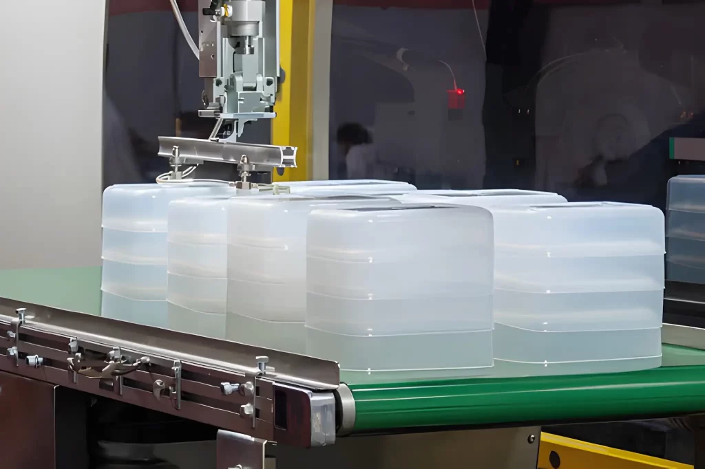 Close-up of a robotic arm handling a plastic food container during the injection molding production process.