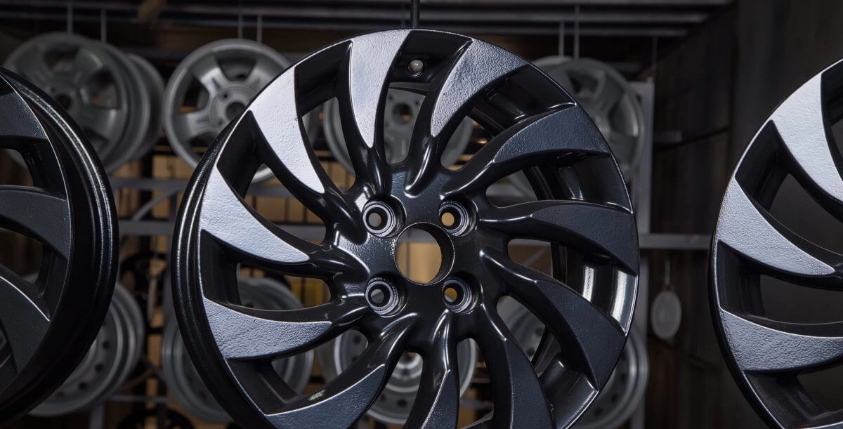 A black powder coated automotive alloy wheel photographed against a dark background
