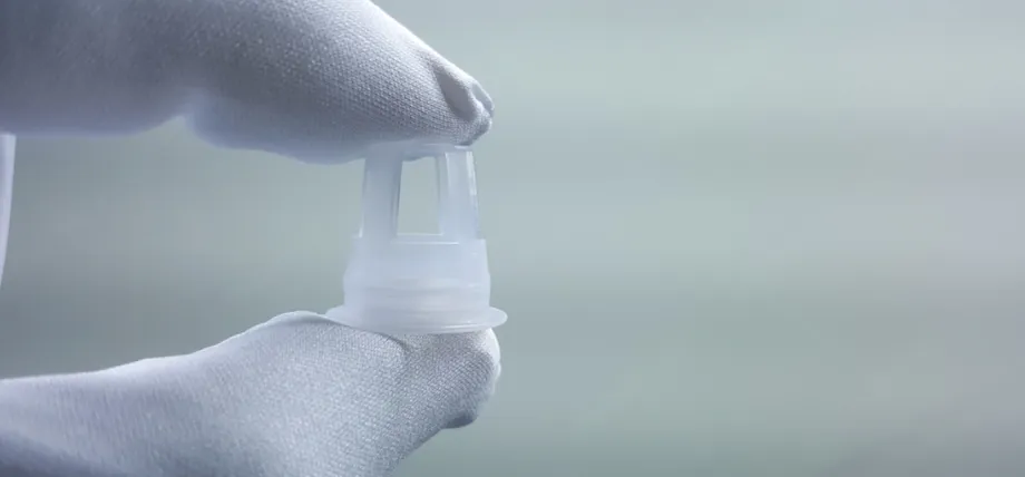 A gloved hand holds a tiny, translucent injection-molded plastic component to demonstrate its precise detail and small scal
