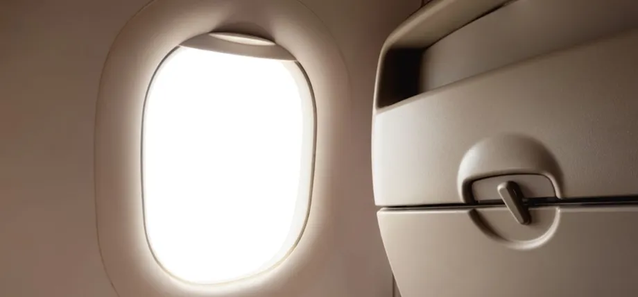An airplane cabin interior showing the smooth, contoured plastic injection-molded window frame and adjacent tray table housing.