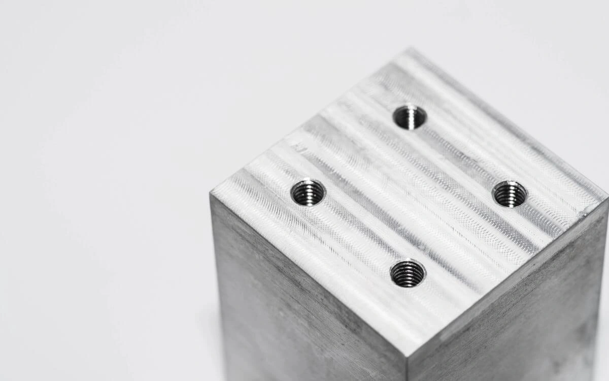 A machined aluminium plate with a pattern of drilled and tapped holes