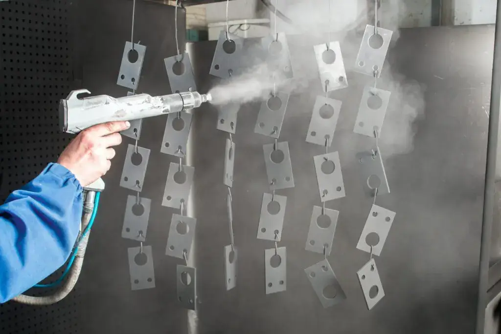 An operator hand spraying Teflon paint on hanging steel parts