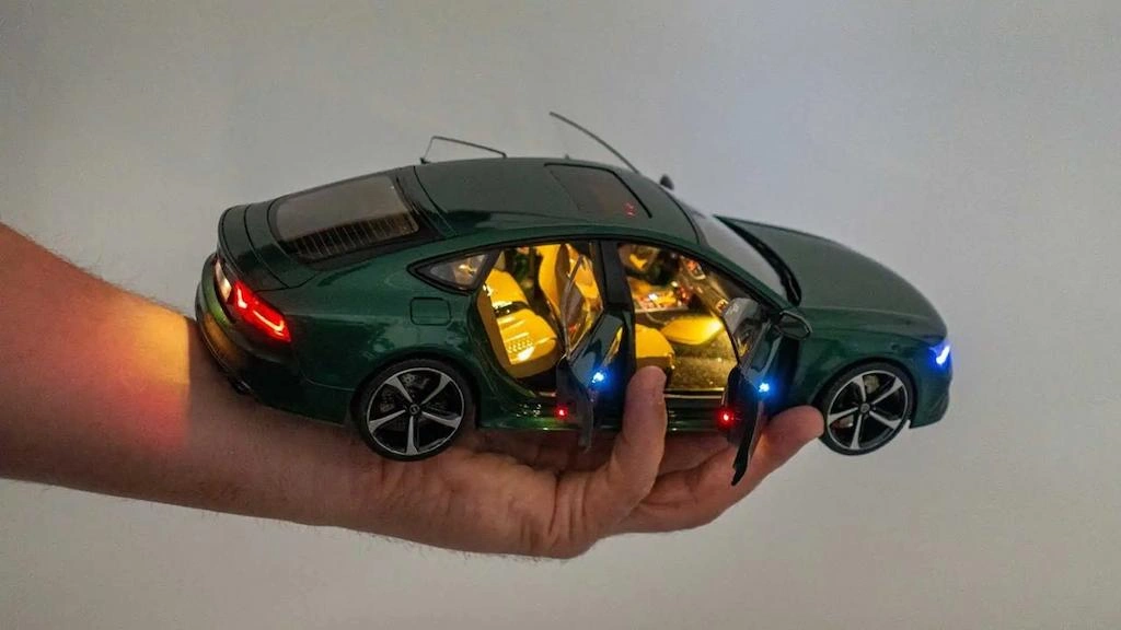 A hand holding model car, open door with light showing interiors