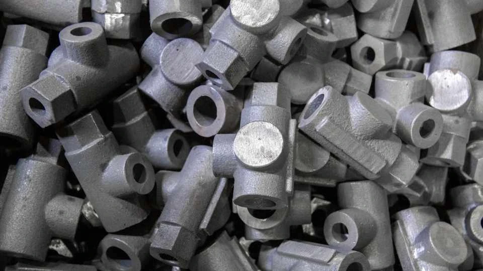 An image showing a bulk stock of zinc die-cast parts, specifically similar pipe elbow-like components. The parts are uniform in shape and size.