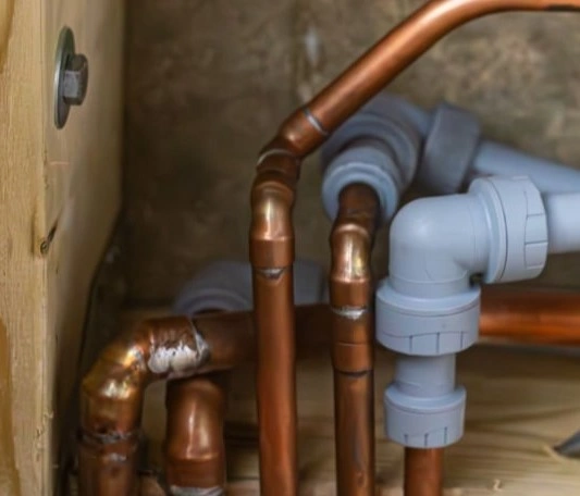 A group of brownish copper pipes and grey plastic pipes connected by T-joints 