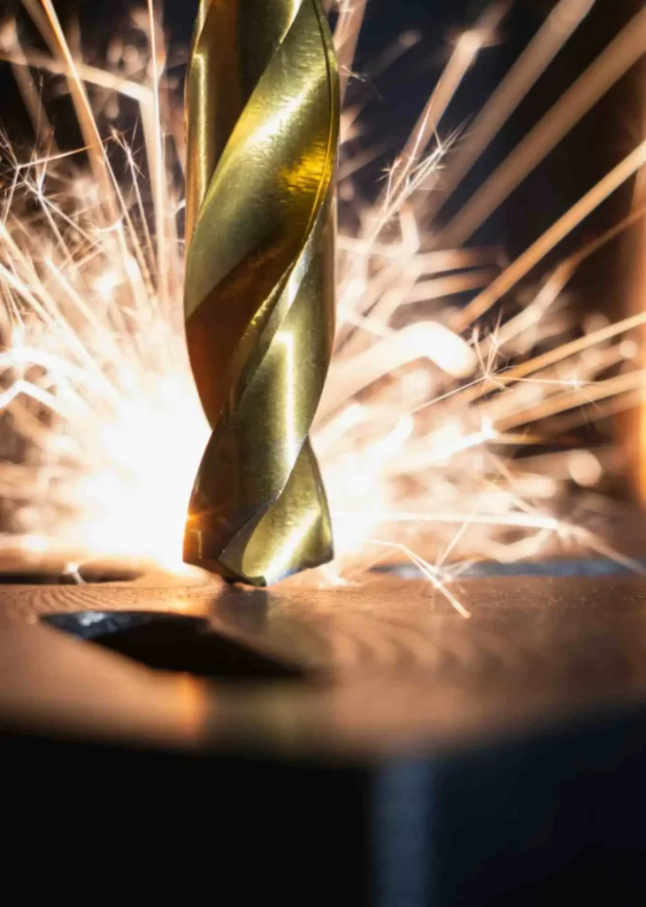 A golden machining tool touching a metallic surface with bright sparks coming out 