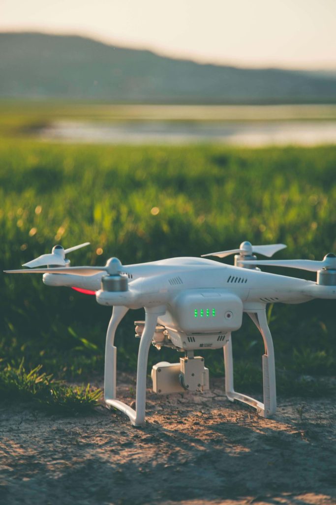 A white drone affixed with a camera resting on the ground 