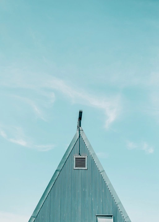 A triangular roof with a small square vent under a clear blue sky