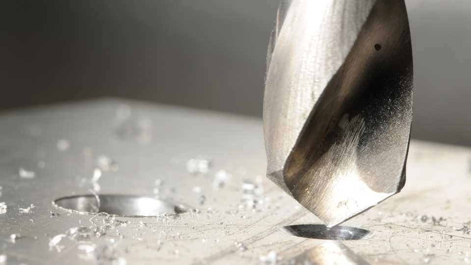 A close-up view of a CNC machine performing hole tapping on a metal workpiece, with precise threading visible inside the drilled hole.