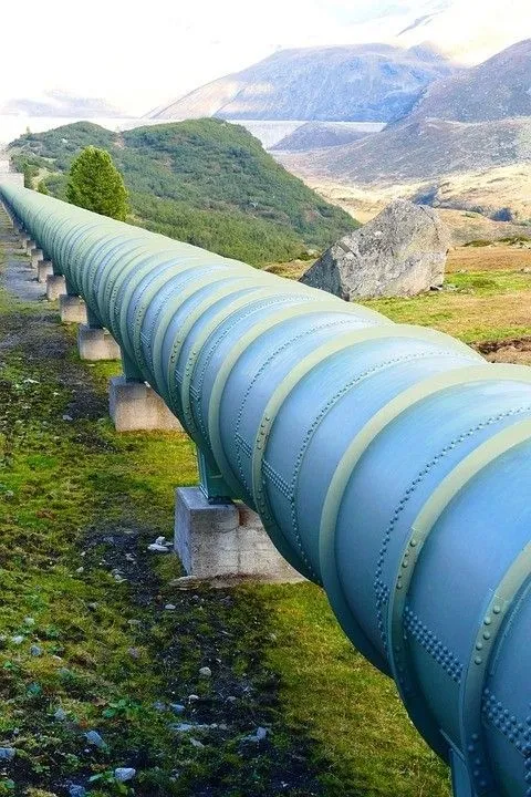 A large blue pipeline of metallic sections riveted together running through a countryside