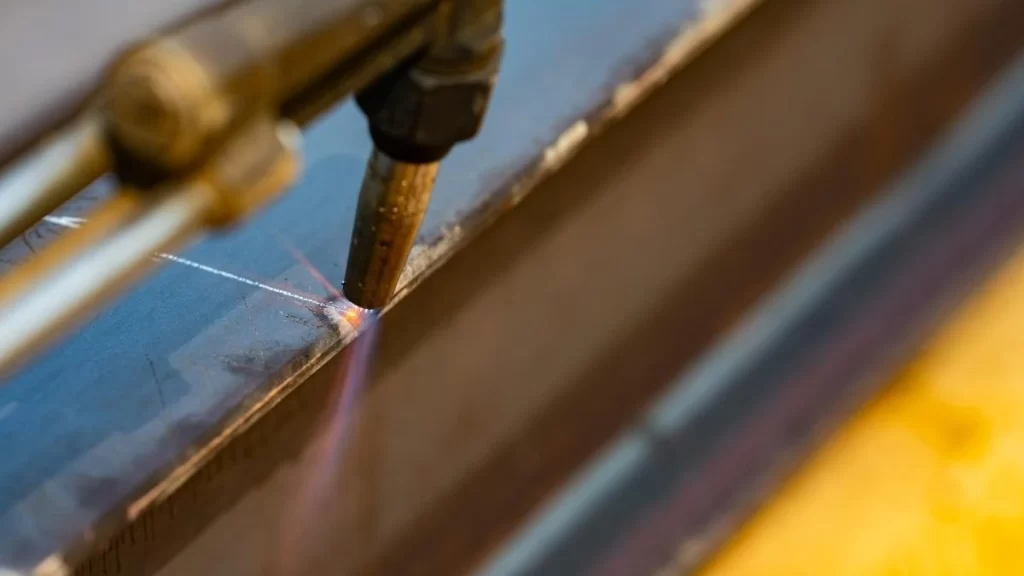 The image shows a plasma cutting machine in operation, using a high-temperature plasma arc to cut through a metal sheet. The process is characterized by bright sparks and intense heat, with the plasma torch.