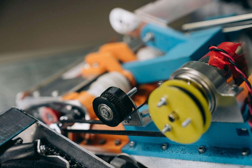 A closeup photo of a mechanism showing two plastic wheels, belt, and wiring