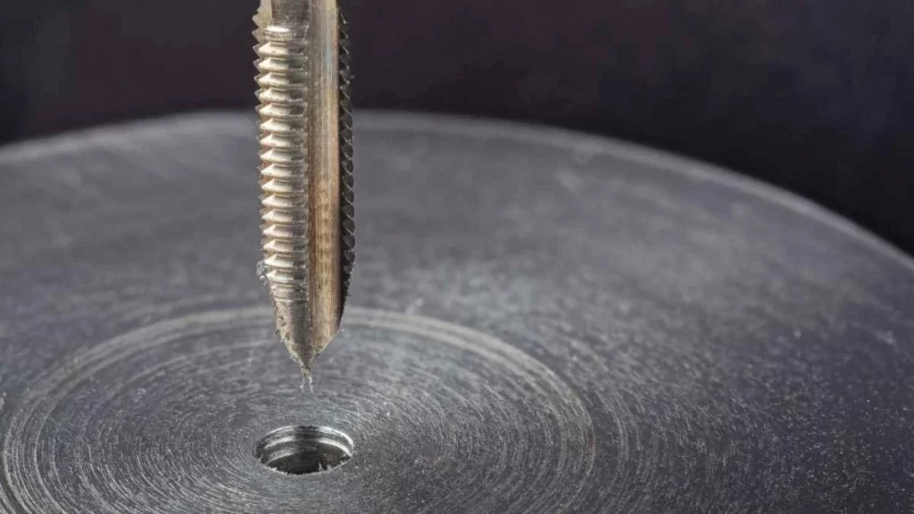 Image of thread tapping process, where a rotating tool creates internal threads inside a hole in a workpiece.