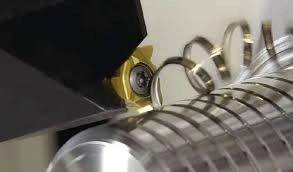 A cutting tool removing chips from a metal shaft as it creates grooves