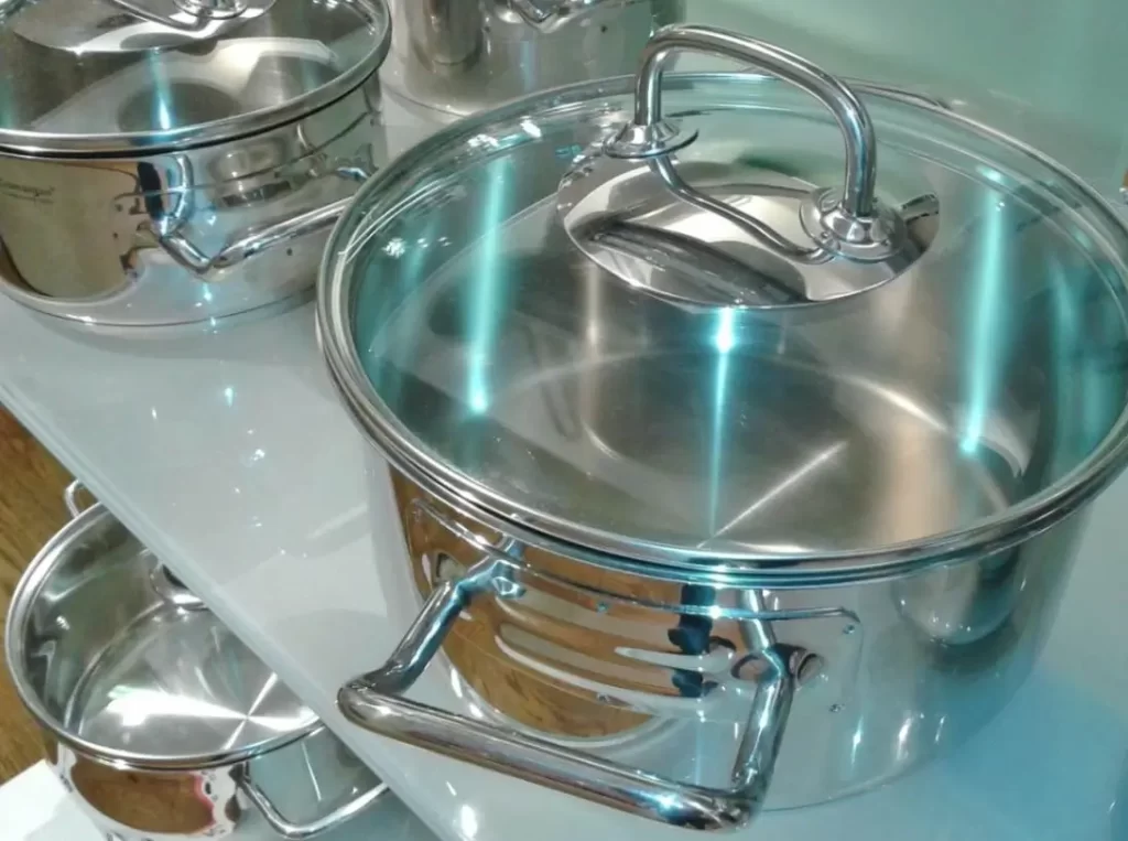 Two shiny silver-colored cooking pots on a table and another pot on the floor