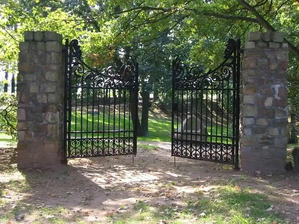 A black metallic gate with flowery decorations partially open leading to a compound