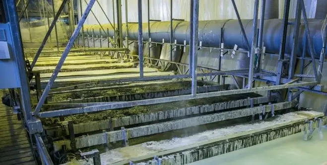 A room with liquid-filled pits surrounded by metallic supports and a large blue pipe on one side