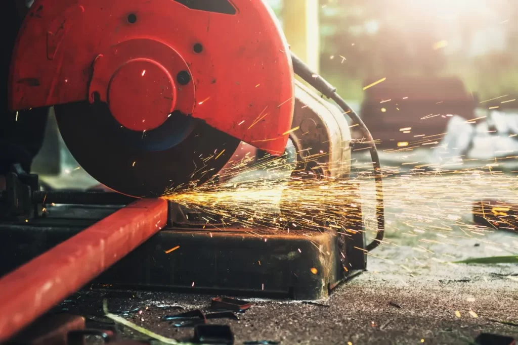 A grinder with a red cover cutting a metal bar and producing sparks