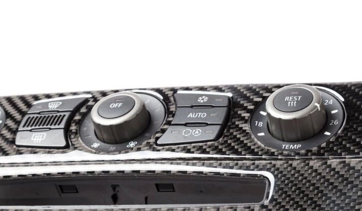 An image of a carbon fiber dashboard of a car showing several knobs sitting on interwoven material