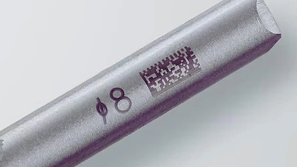 The image showcases a metal part with laser carbon migration markings, displaying dark, high-contrast text.