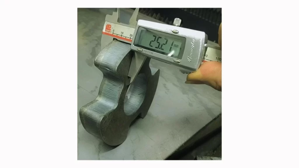 A machinist using a digital scale to measure the thickness of a laser-cut metal part.