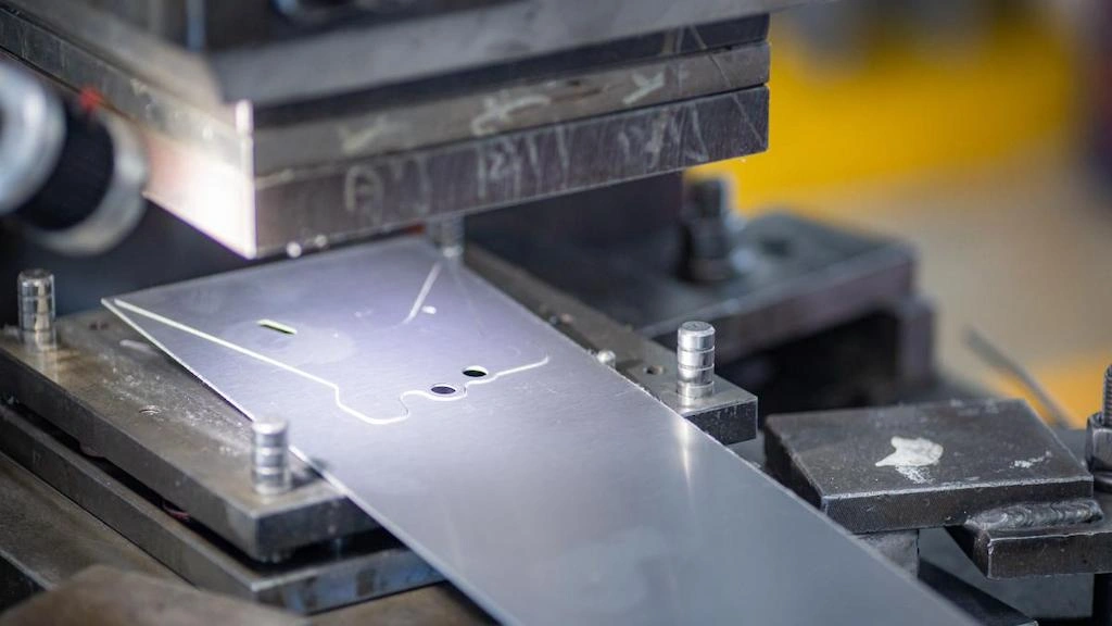 A close-up view of loading sheet into stamping die, holes, and marking on sheet’s surface.