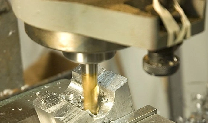 An end mill removing material from a metal block held between jaws