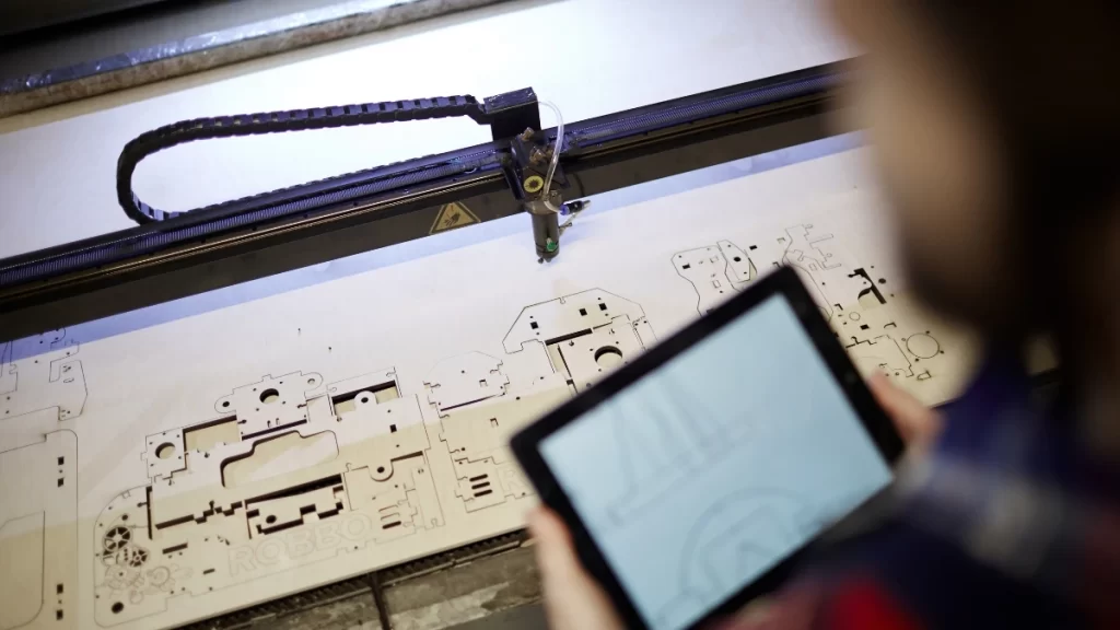 A man standing by a laser cutting machine, controlling the operation to optimize the cutting of stainless steel.