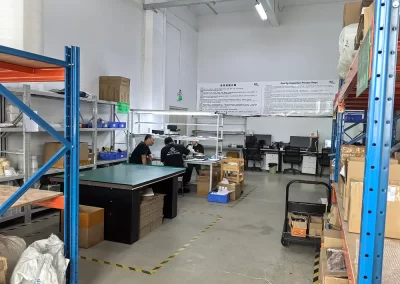 The image shows the factory's packaging room, with a packaging table in the center, along with related packaging materials and computer data entry equipment.