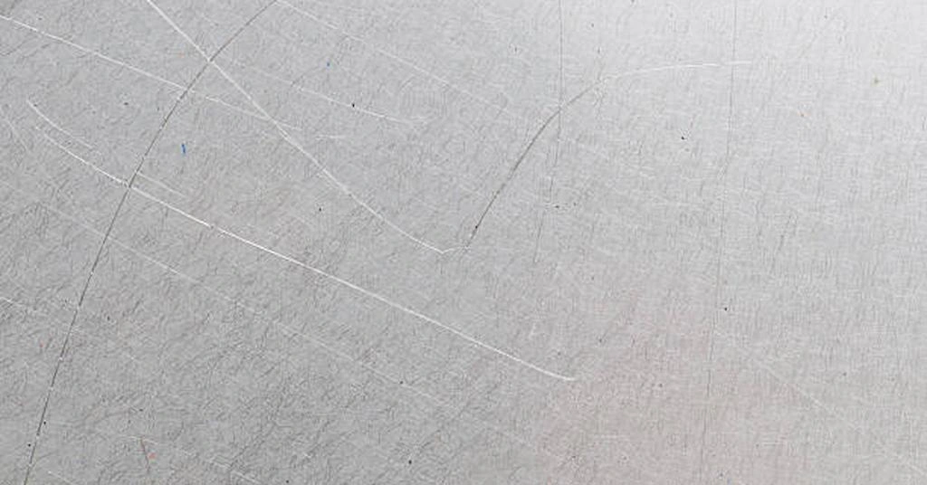 A close-up view of a steel sheet with scratches on the surface, showing material defect example in stamping 