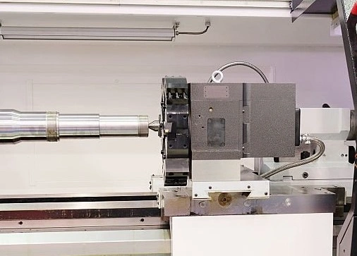 An image of a carriage showing metallic CNC lathe components on a rail with a turret linking to a cylindrical workpiece