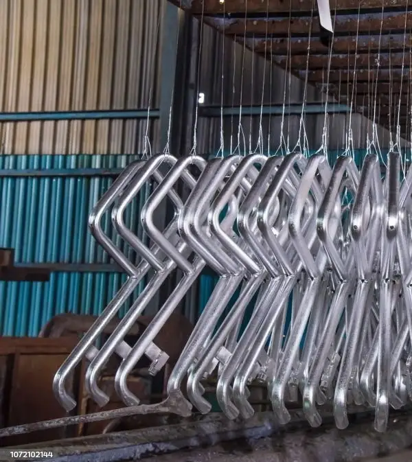 An image of metal parts undergoing hot-dip galvanizing, suspended on hooks in an industrial facility.