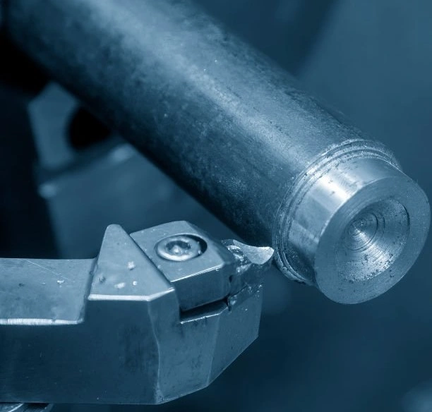 A closeup image of a metal shaft being machined by a sharp-tipped tool