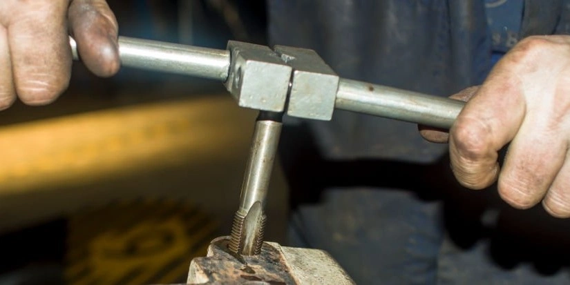 A closeup image of a person using a tap wrench to create internal threads in a metal component 