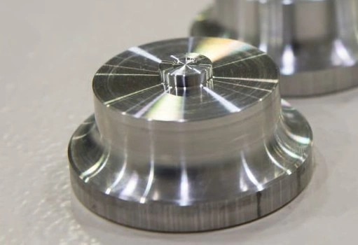 An image of a machined button-shaped metal component with visible tool marks on its surface