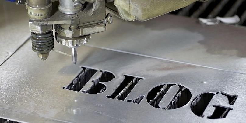 A machine with a nozzle directed on a metal sheet with the word “BLOG” engraved on the metal sheet