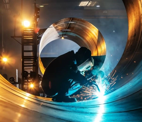 A closeup image of a welder joining two pieces of sheet metal with sparks and a bulb light in the background