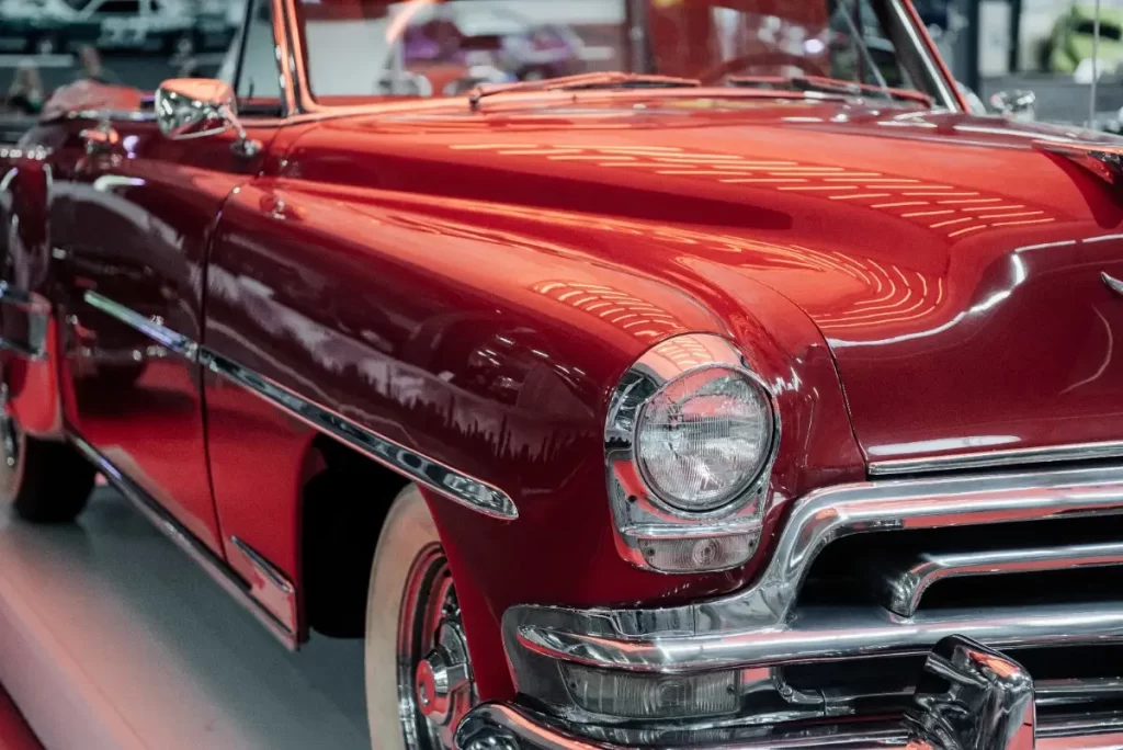 A close-up of an antique red car with detailed exterior features such as a front lamp