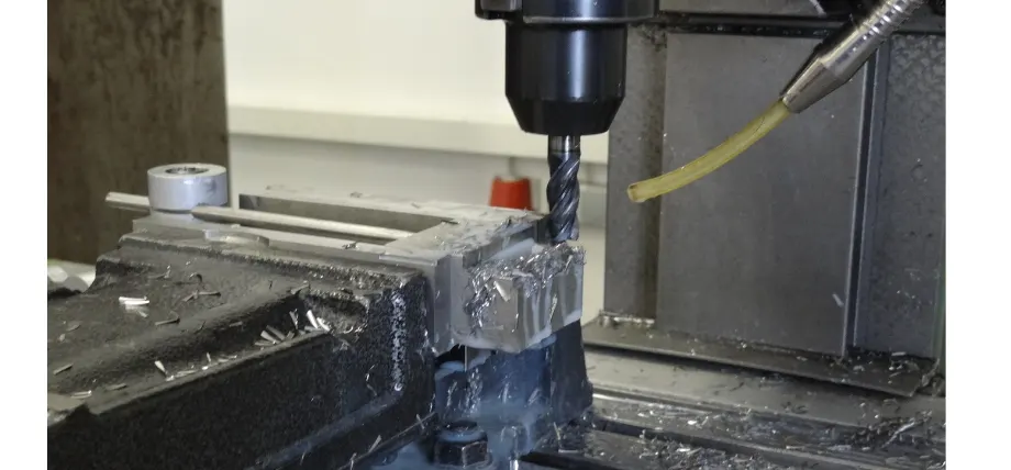 Milling cutter chipping off a layer of metal with coolant flowing over the workpiece