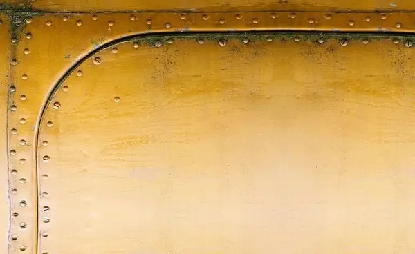 A closeup view of a yellow aircraft panel, hemmed and riveted