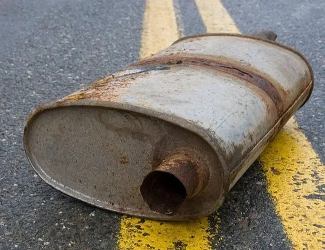 A rusted muffler lying on an asphalt road with faded yellow dividing lines